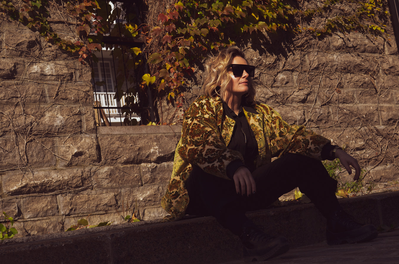 Photo of female model sitting on the sidewalk wearing the House of Glass Carpetbag Bomber Jacket