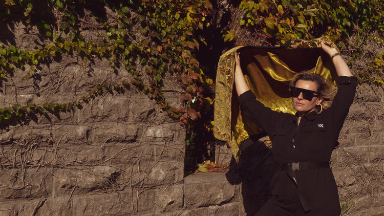 Photo of female model standing in front of an ivy covered wall wearing the House of Glass Carpetbag Bomber Jacket