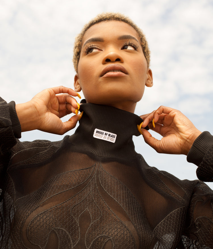 Picture of female model wearing black Hot Mesh Dress lifting the collar to show house of glass patch detail