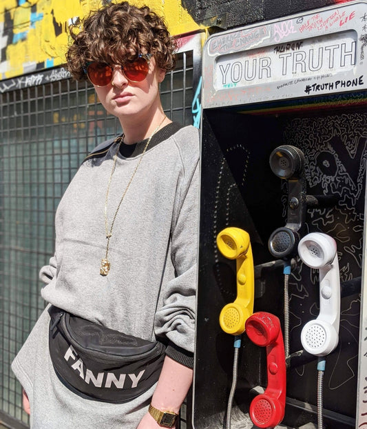 picture of non binary model looking into the camera wearing house of glass cozy comfy sweater beside telephone booth art installation
