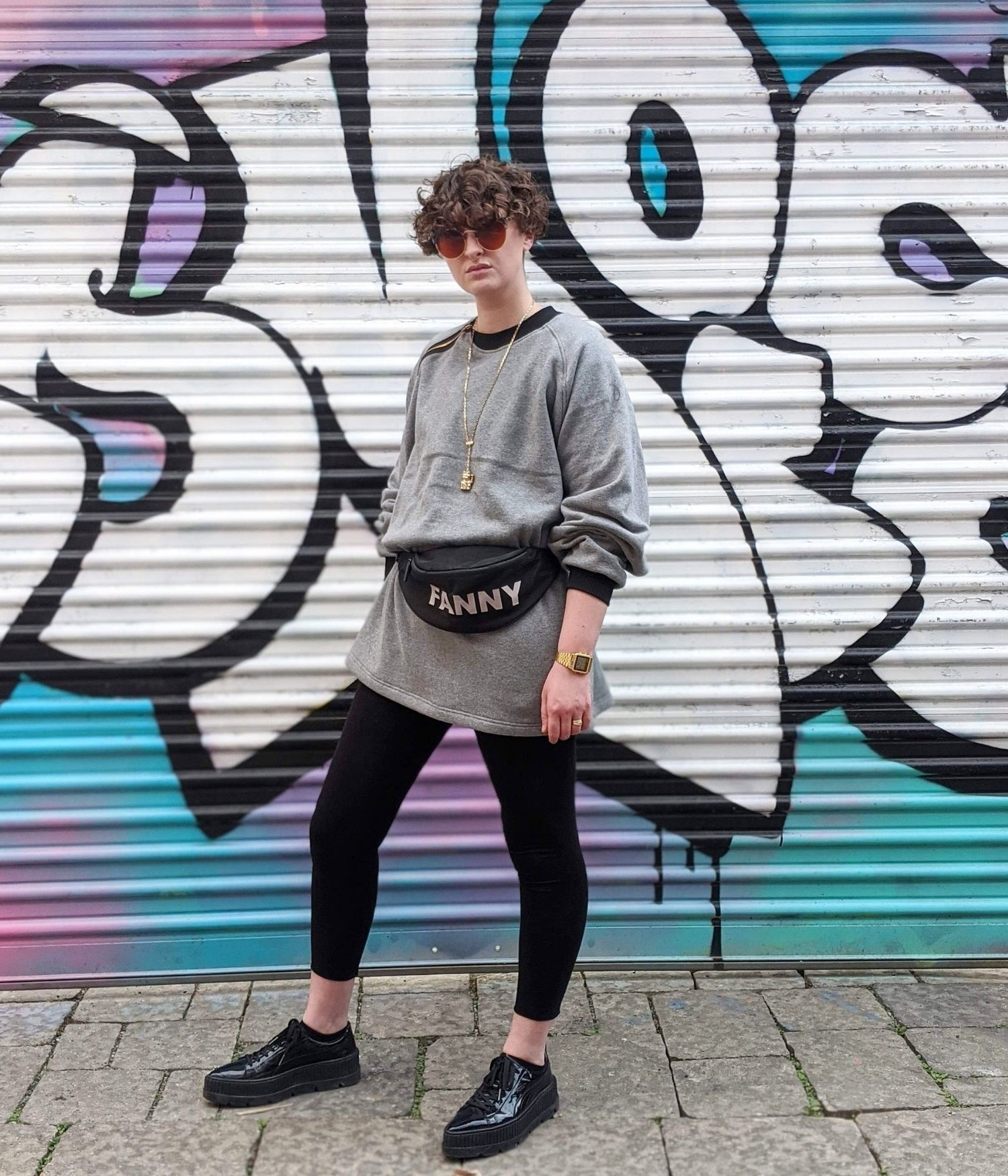 picture of non binary model looking into the camera wearing house of glass cozy comfy sweater standing in front of graffiti covered garage door