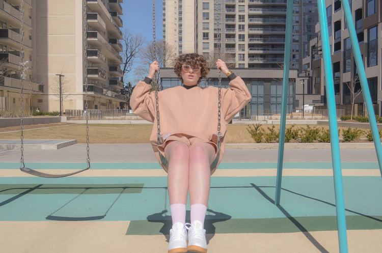 picture of non binary model sitting on swing set wearing halfsuit in pink