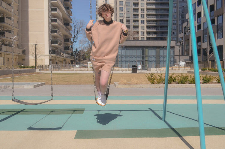 picture of non binary model standing on swing set wearing halfsuit in pink