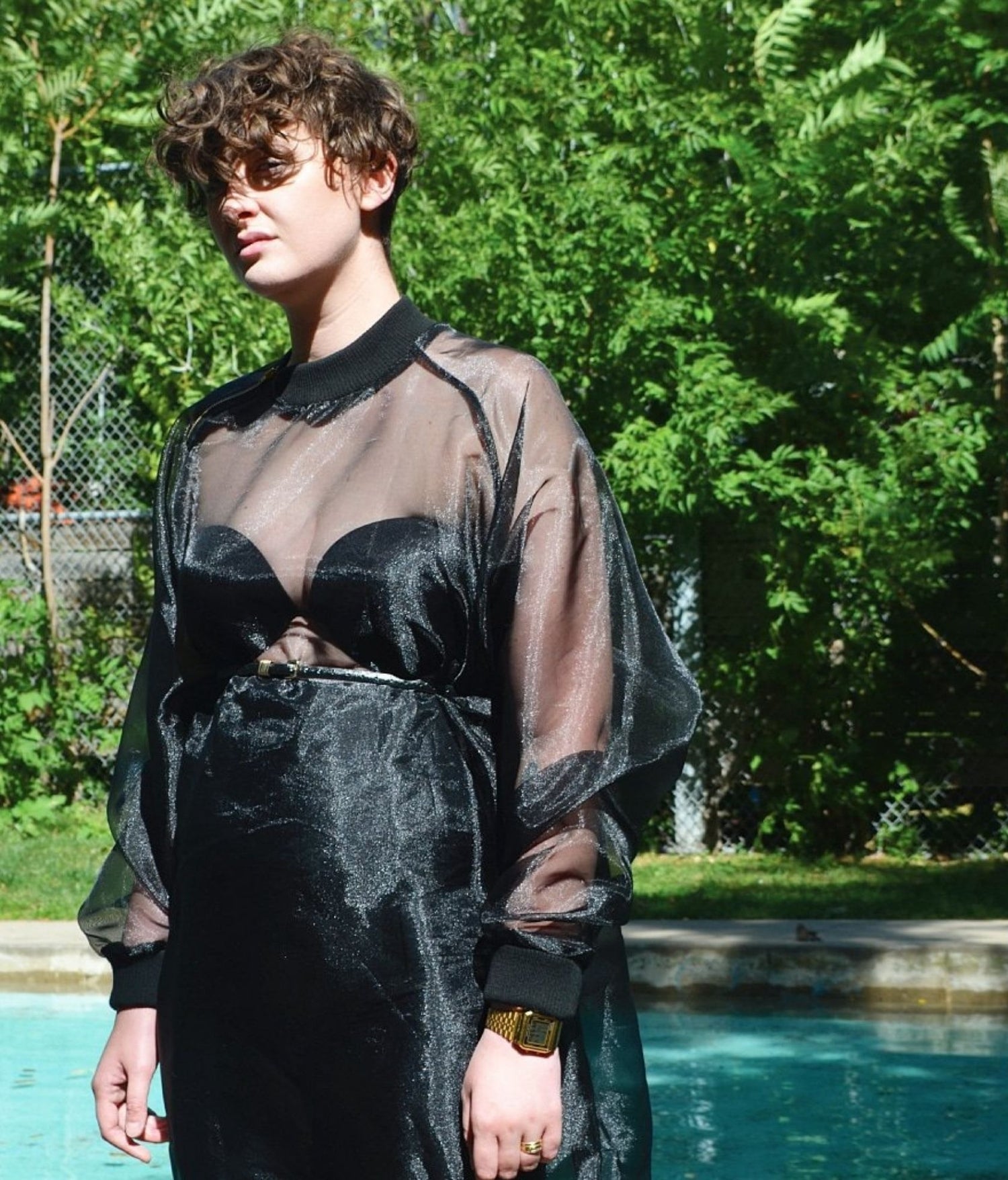 picture of non binary model wearing house of glass long black organza jumper standing in front of swimming pool