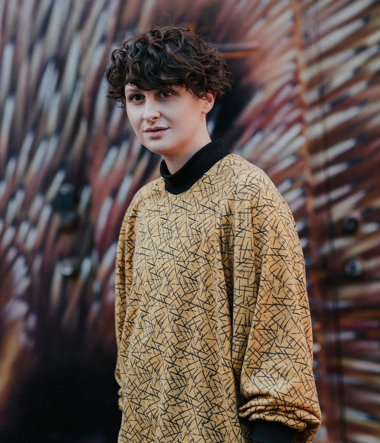 picture of non binary model wearing pickup stix jumper in front of graffiti background