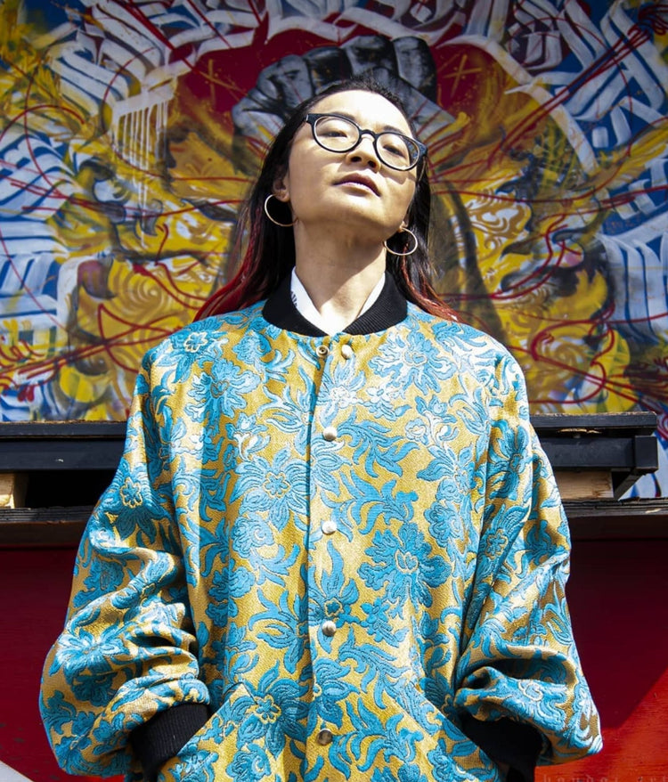 picture of non binary model wearing the house of glass st neot bomber jacket standing in front of graffiti wall