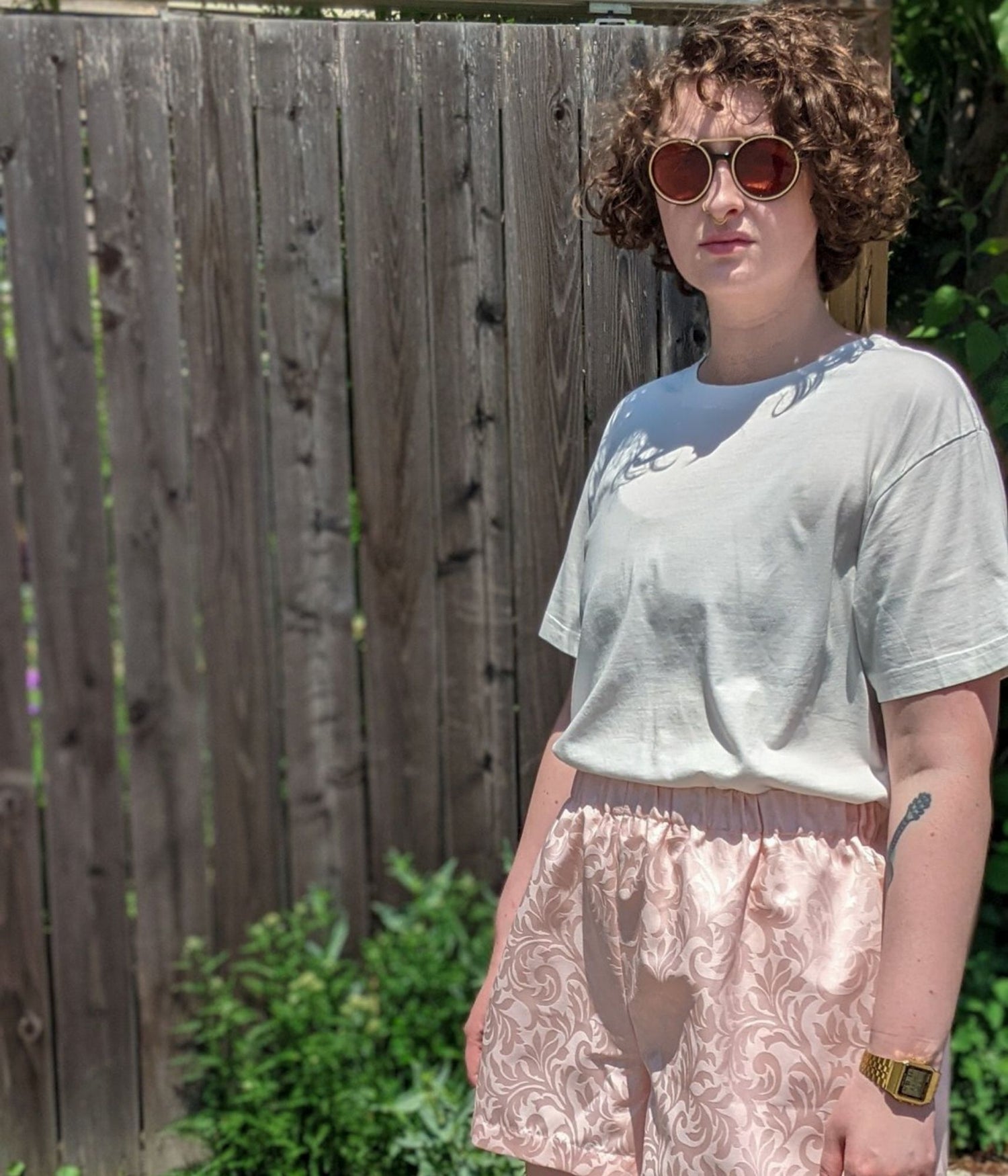 picture of non binary model wearing white t-shirt and Aramis Shorts standing in front of fence