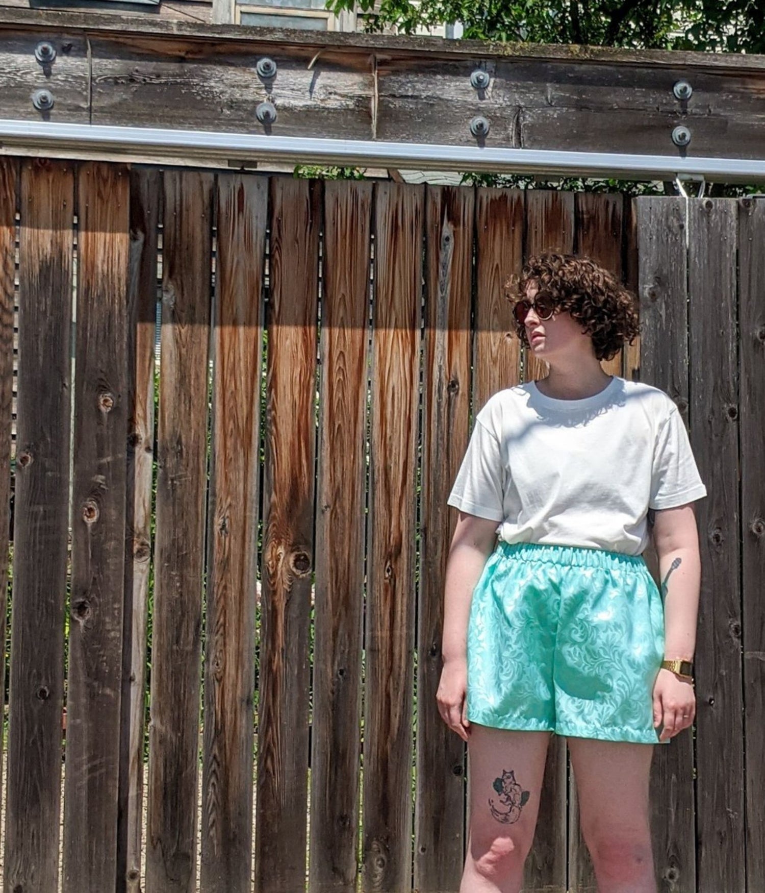 picture of non binary model wearing white t-shirt and Athos Shorts in front of wooden fence