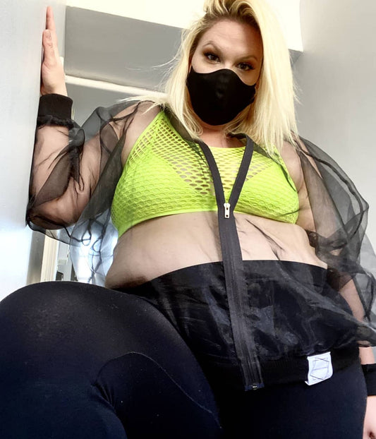 picture of plus size model wearing house of glass black sick organza bomber jacket black mask and neon green bra looking down into the camera